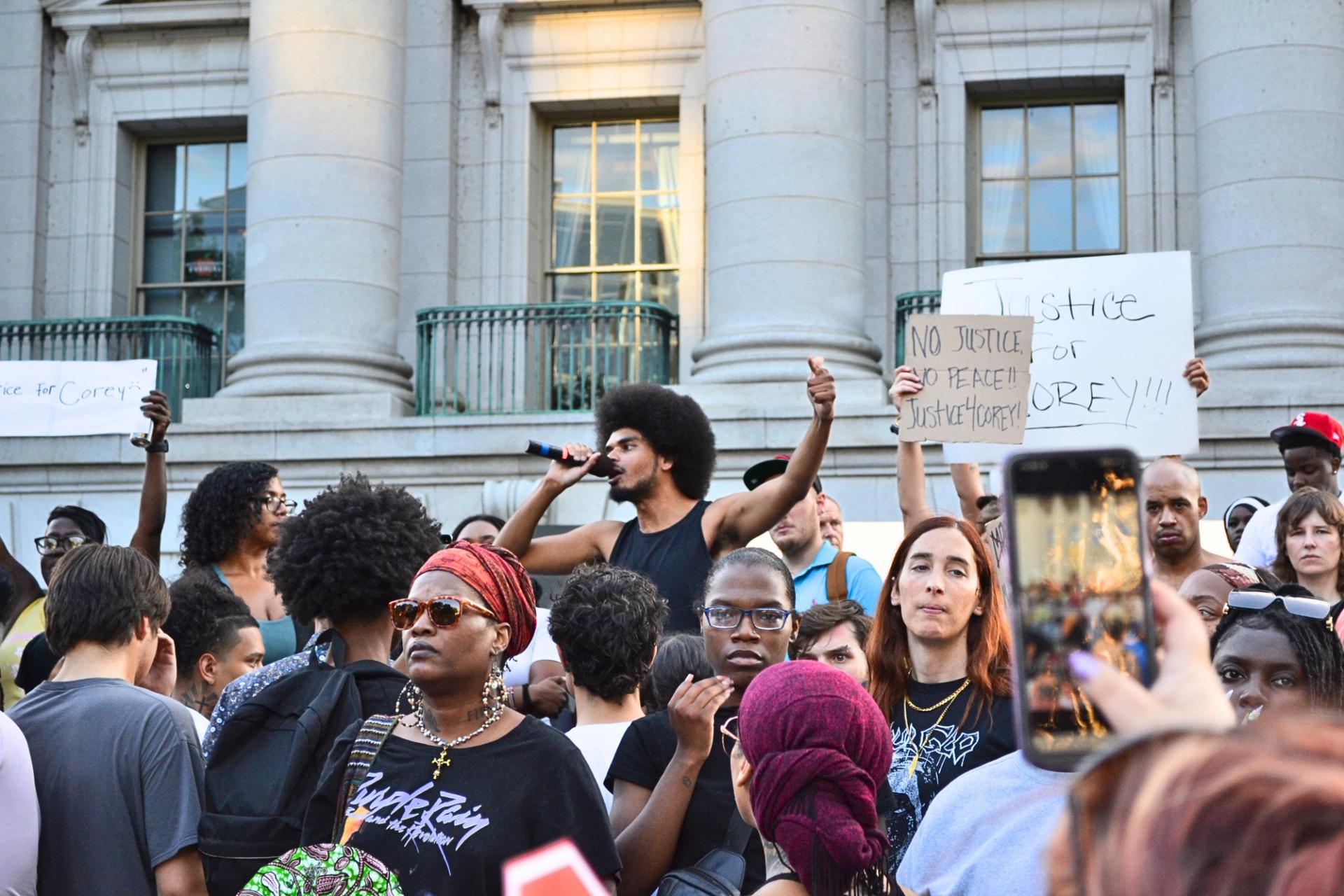A man in a black shirt holds a microphone in a crowd.