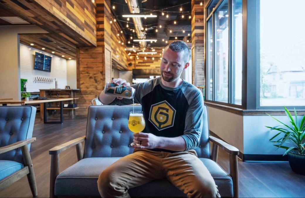A man sitting in a chair pours beer into a glass.