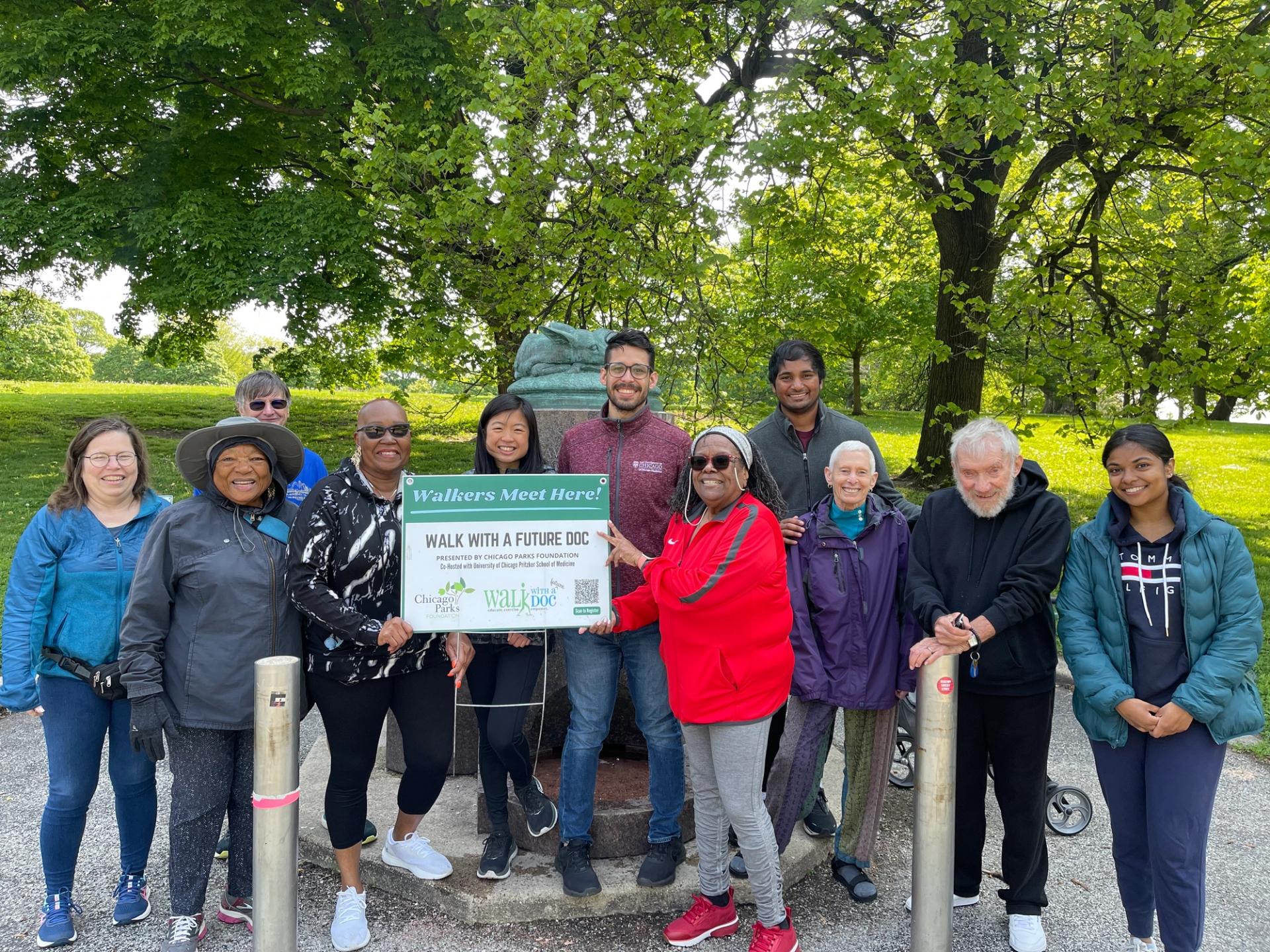 A group of walkers and students stand in a park with a sign that says "Walk With a Future Doc"