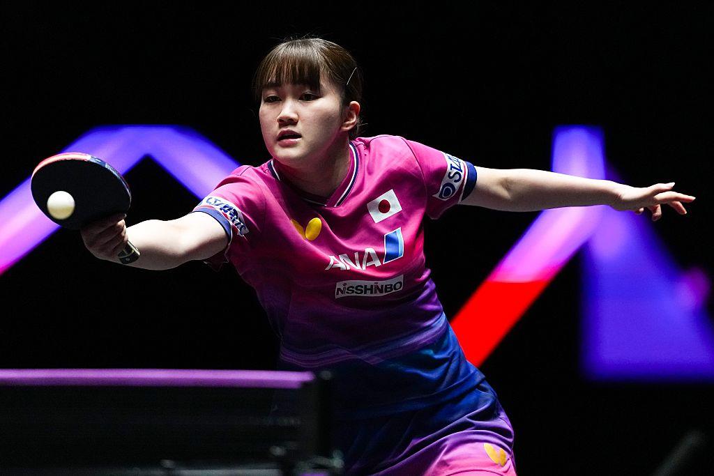 Person hits ball in a table tennis match wearing a pink shirt with purple and black background