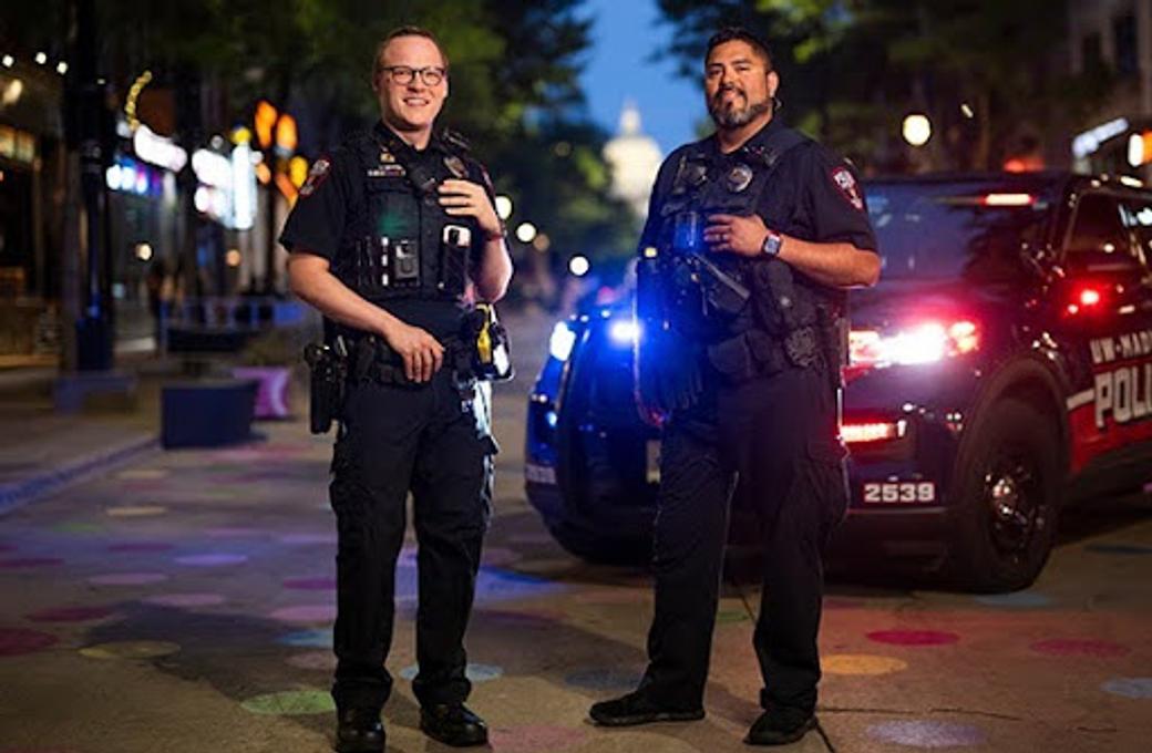 Two police officers stand in front of a police vehicle