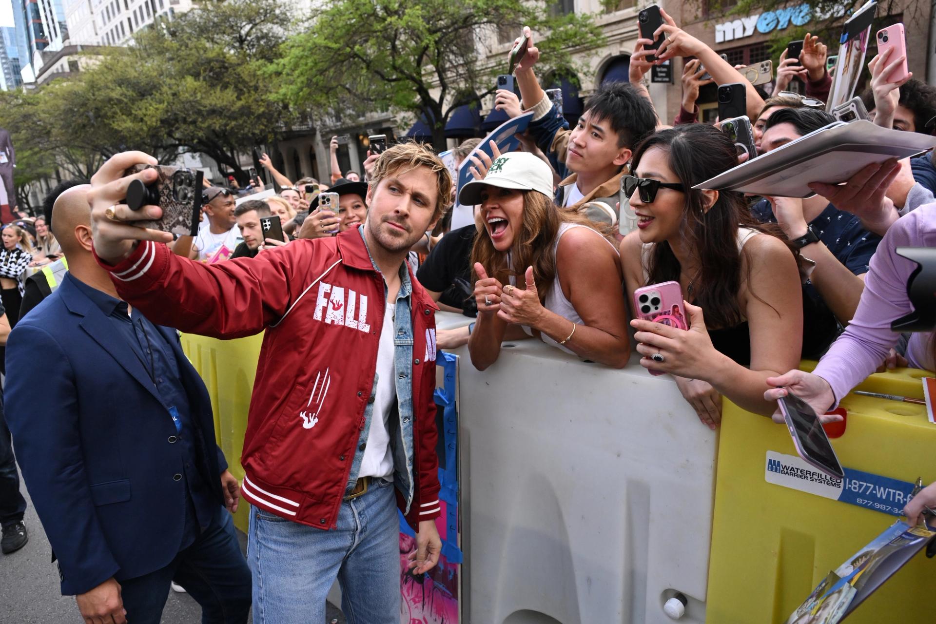 A crowd of fans stands behind Ryan Gosling as he takes a photo with a woman.
