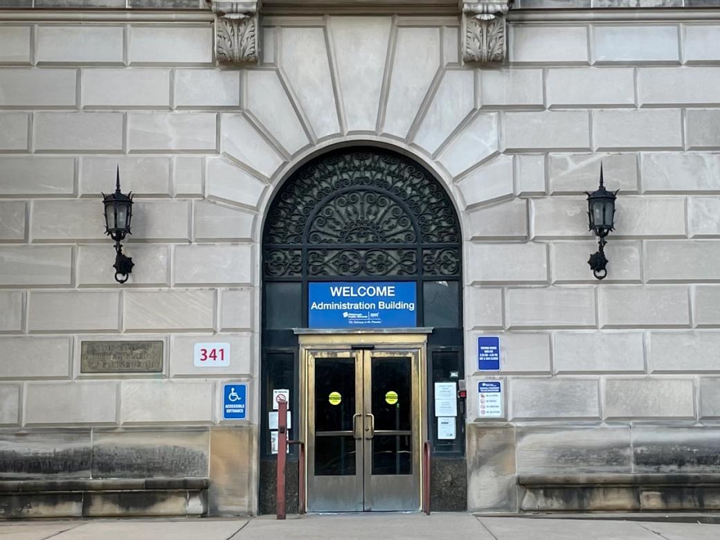 A large stone building with an arched rod-iron design over the exterior door and a sign that says "WELCOME Adminstrative Building"