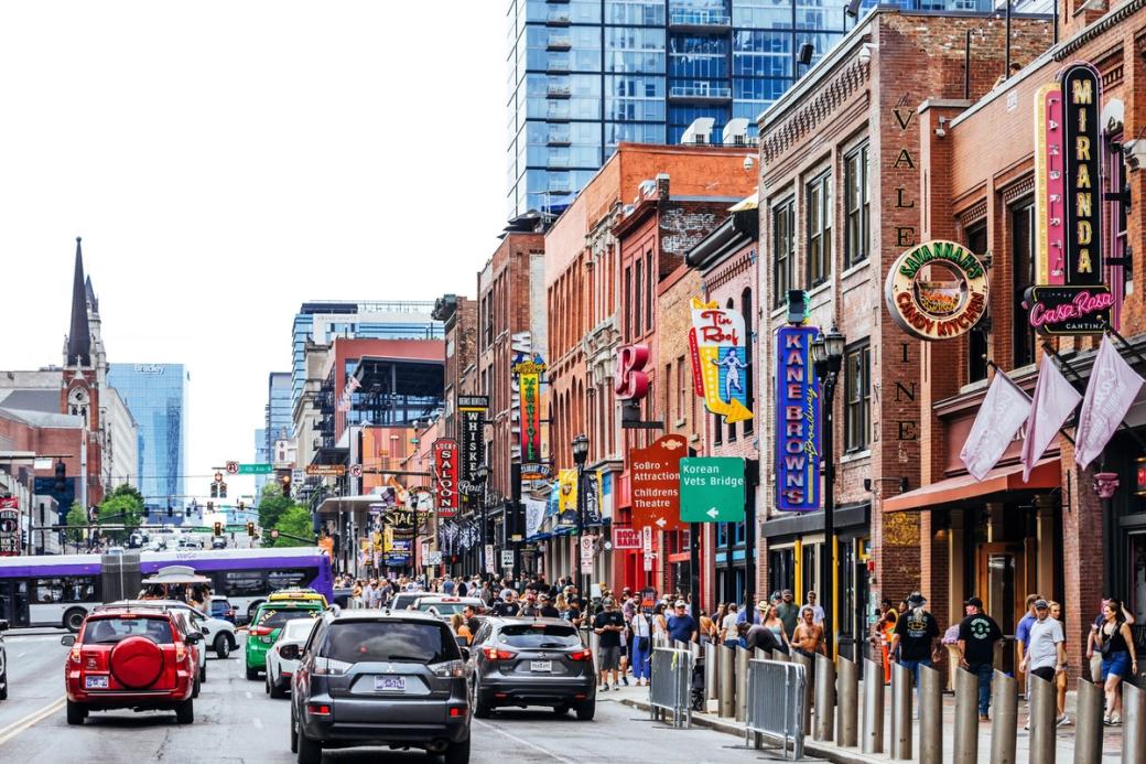 A busy road in downtown Nashville, with lots of pedestrians on sidewalks outside brick honky-tonks.