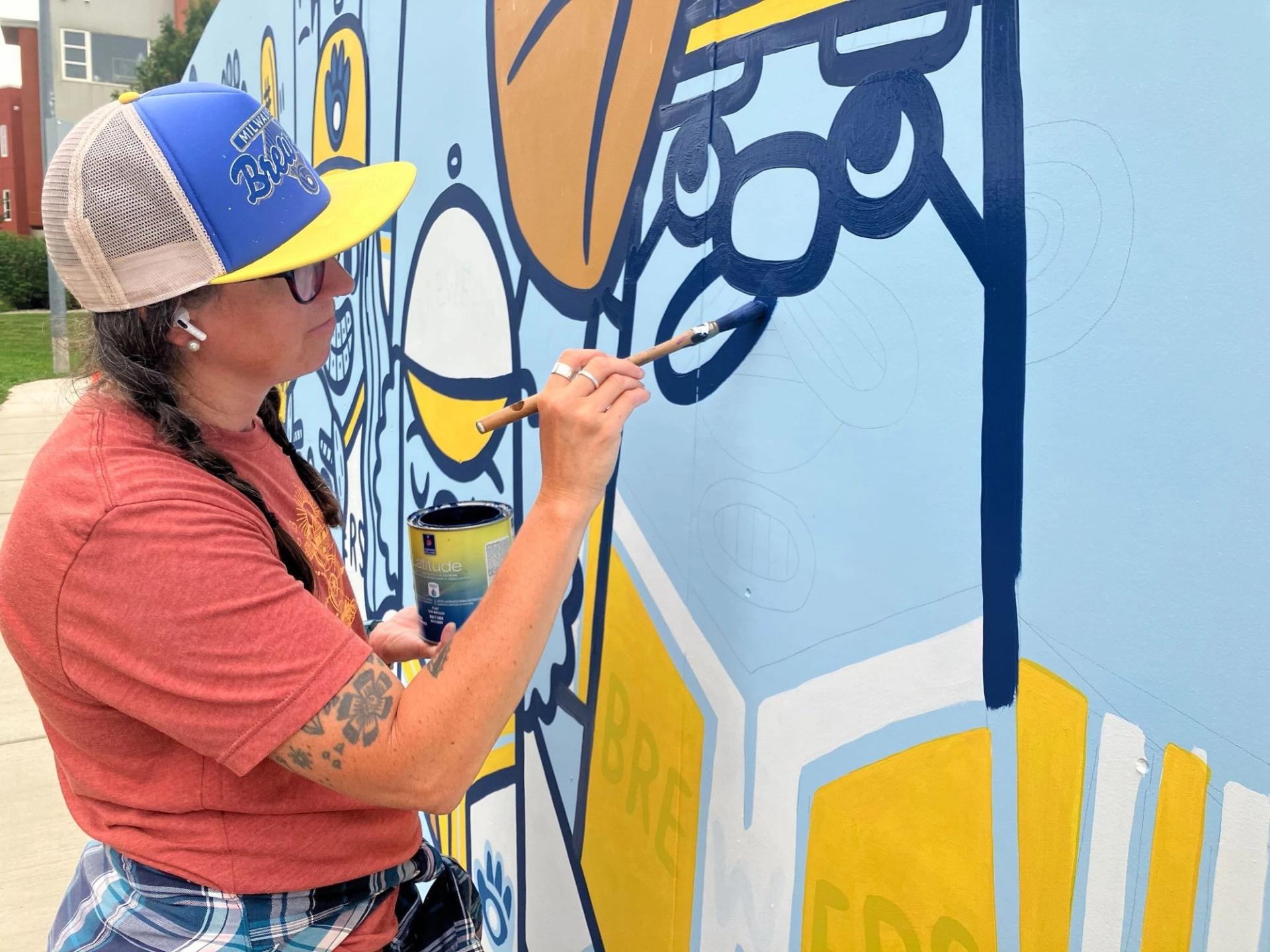 A close up of a woman painting a face on a mrral on a wall.