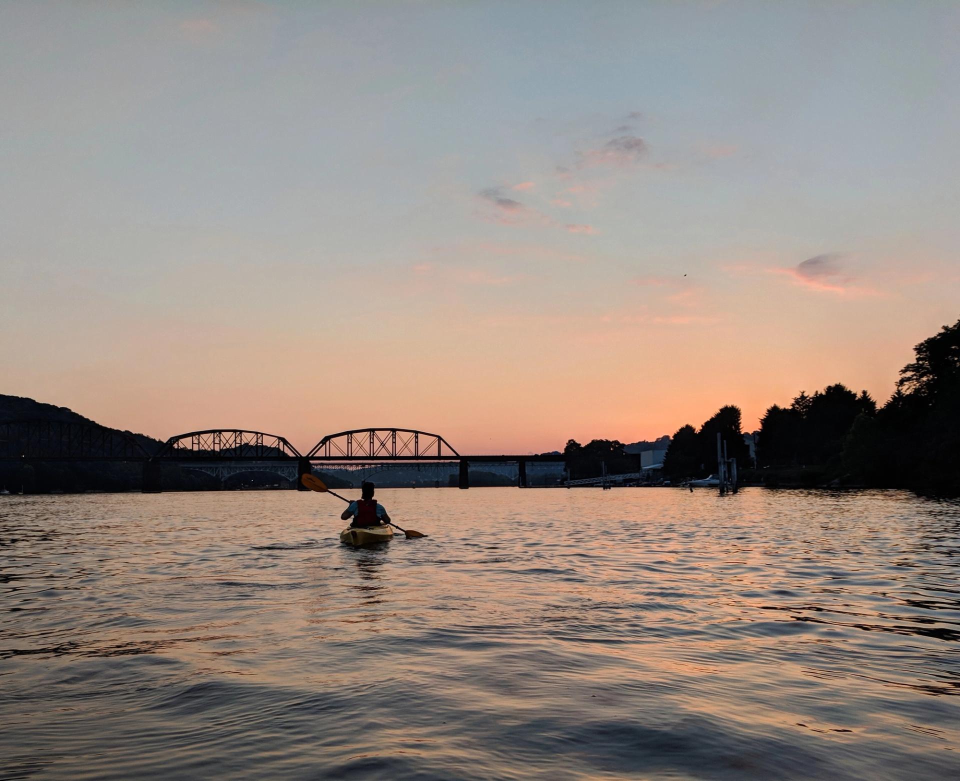 a sunset kayaker with a bridge in the background