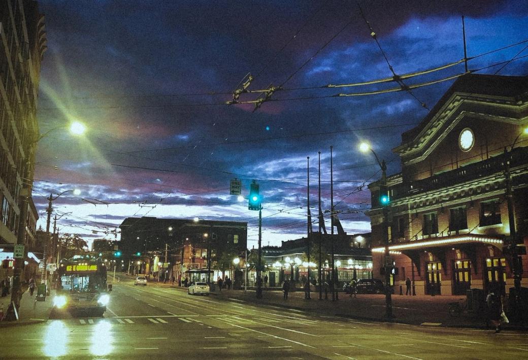 Dark skies over King Street Station in the CID. A bus sits at a stop light across the street with its headlights on.