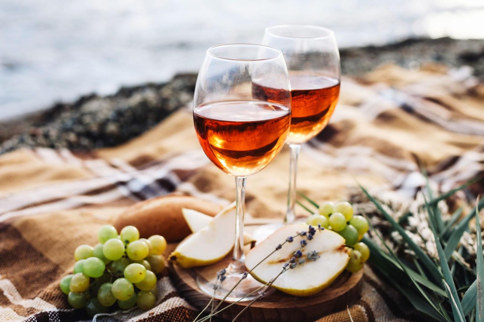 Two glasses of wine sit next to a body of water