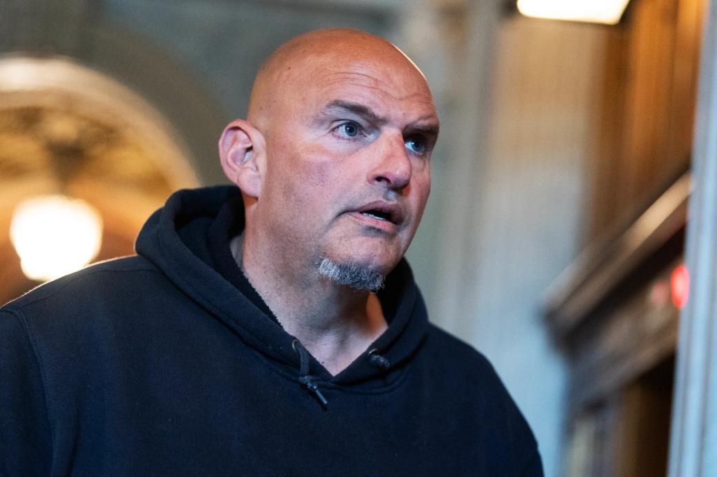 Pennsylvania Sen. John Fetterman, wearing his signature black hoodie, looks intently off-camera in a close-up portrait shot inside the U.S. Capitol.