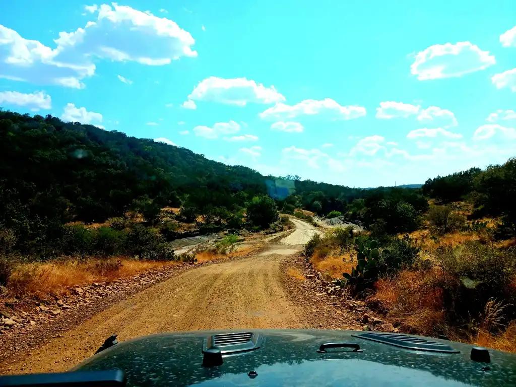A dirt road between two hills covered with green trees.