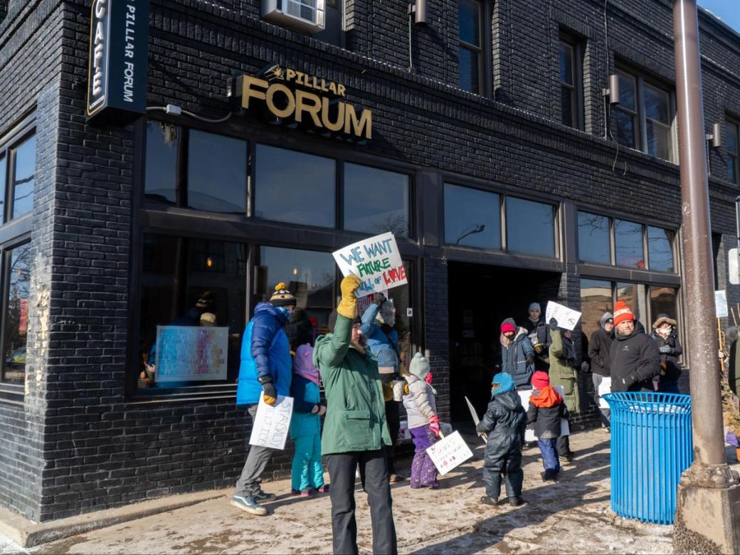 A protester holds a sign reading "we want a future full of love" outside of Pilllar Forum in January. Other protestors are visible in the background.