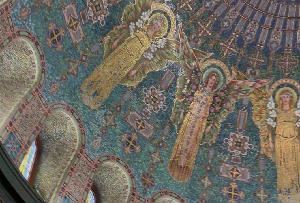 Looking up at colorful tile mosaic on interior of domed ceiling, including angels and intricate designs