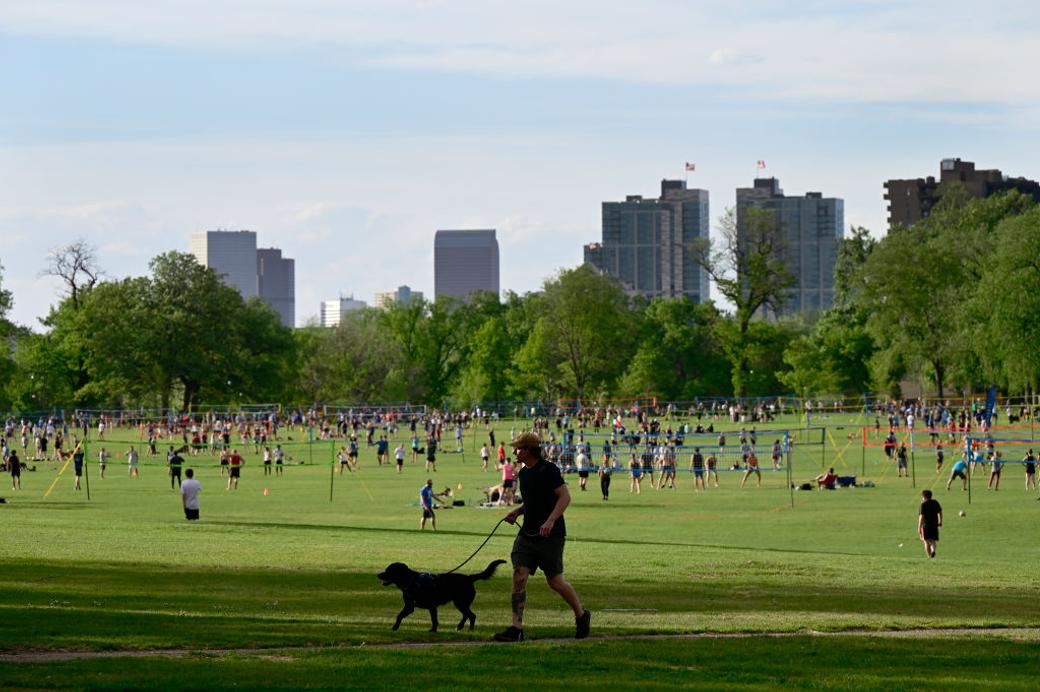 People enjoy a park and a person walks a dog with cityscape in the background