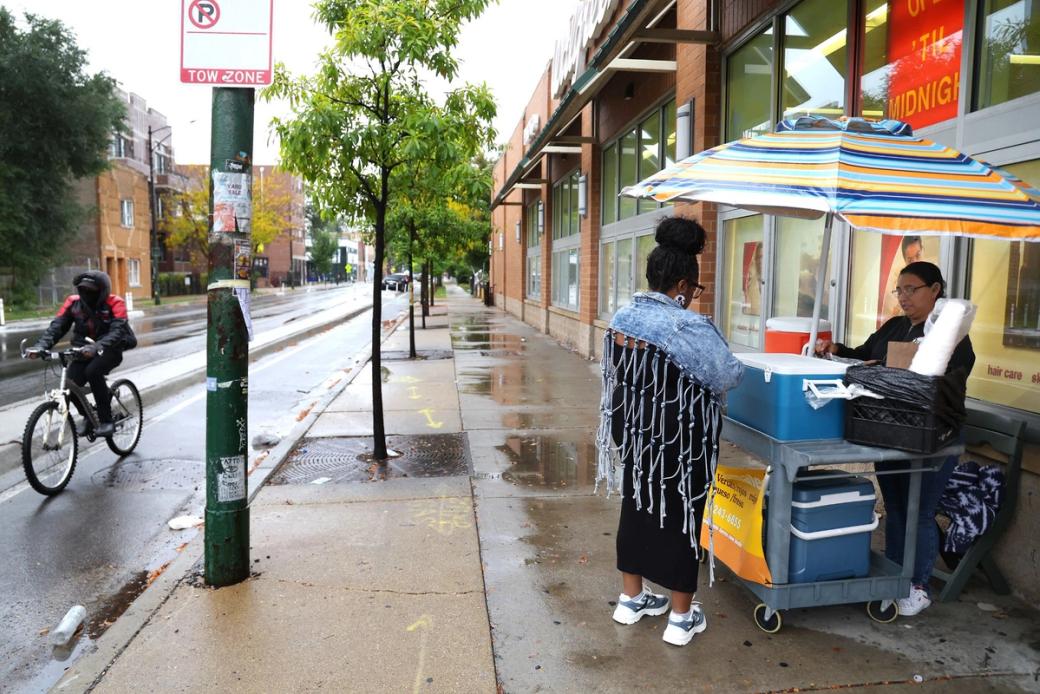 A street vendor bags tamales for a customer along a mostly empty city street.