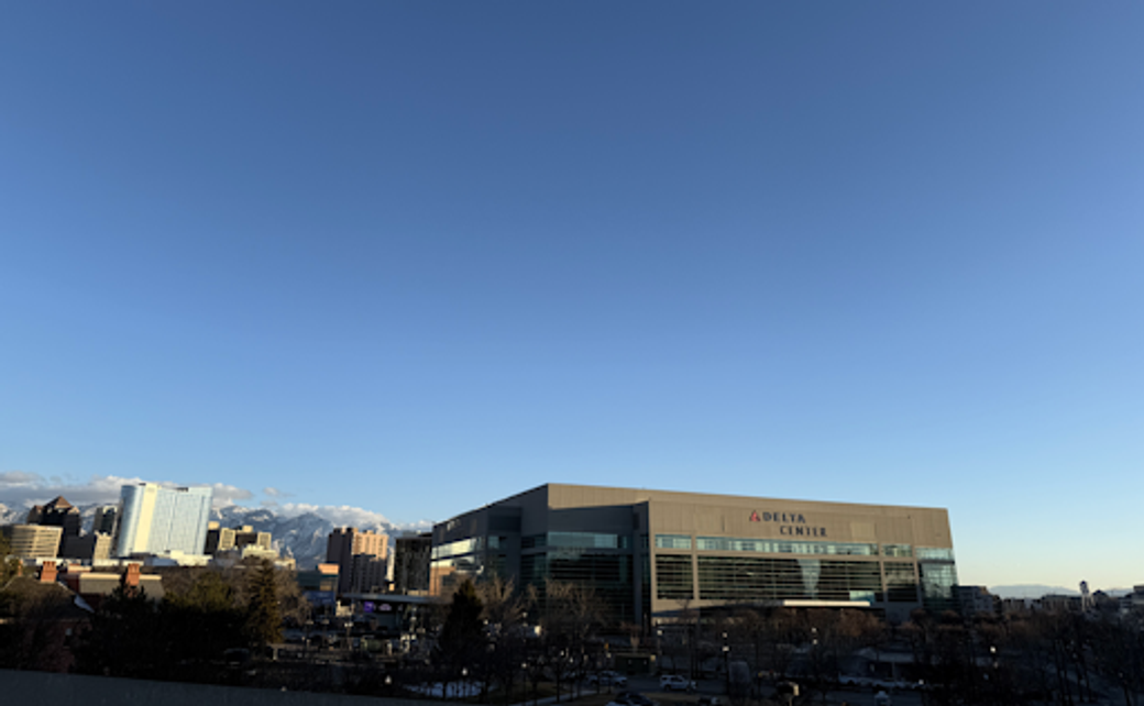 Exterior of Delta Center and downtown Salt Lake City buildings, with mountains in the background.