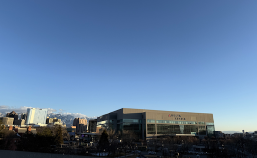 Exterior of Delta Center and downtown Salt Lake City buildings, with mountains in the background.