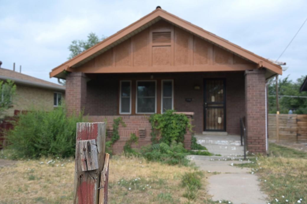 Exterior of a brown brick abandoned home, with grass and bushes overgrown