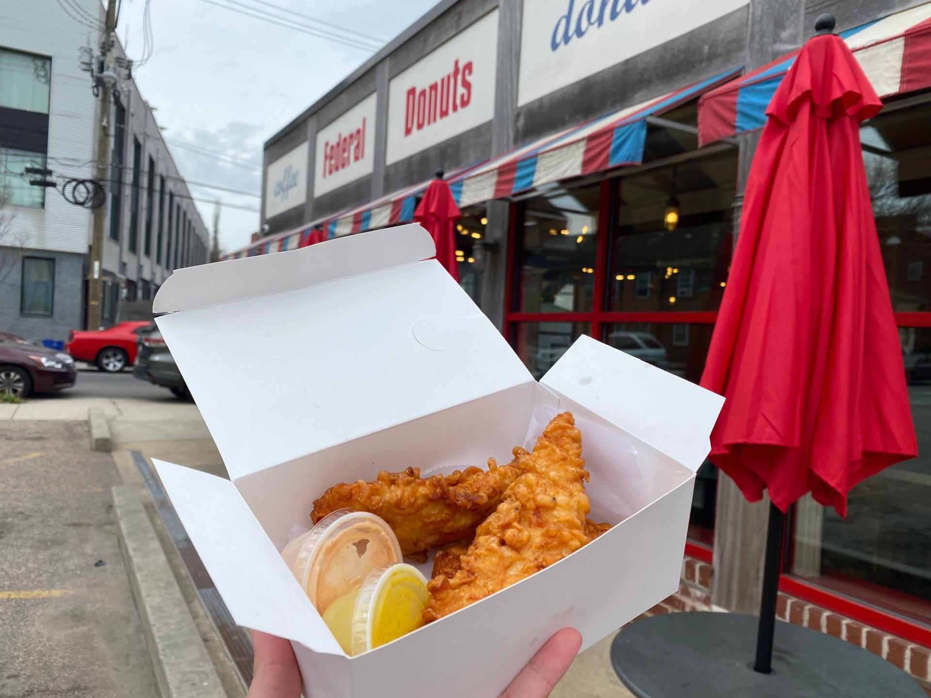 A box of chicken tenders in front of a Federal Donuts storefront.