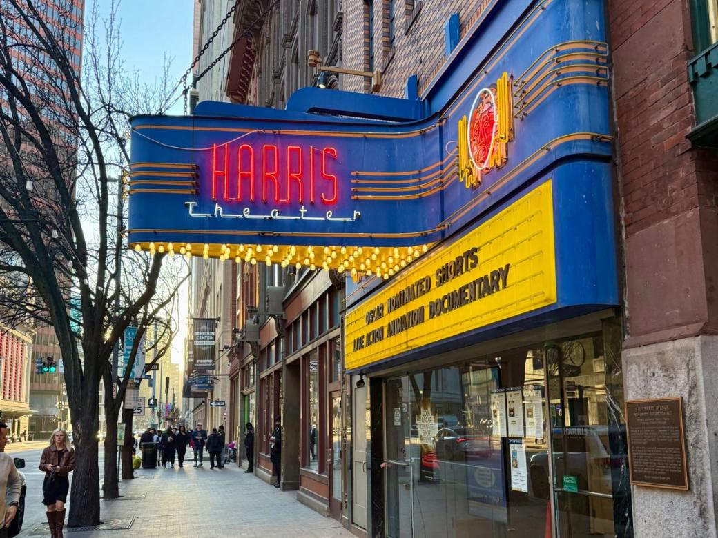 The Harris Theater marquee’s has its name in red neon lights on a bright blue background.