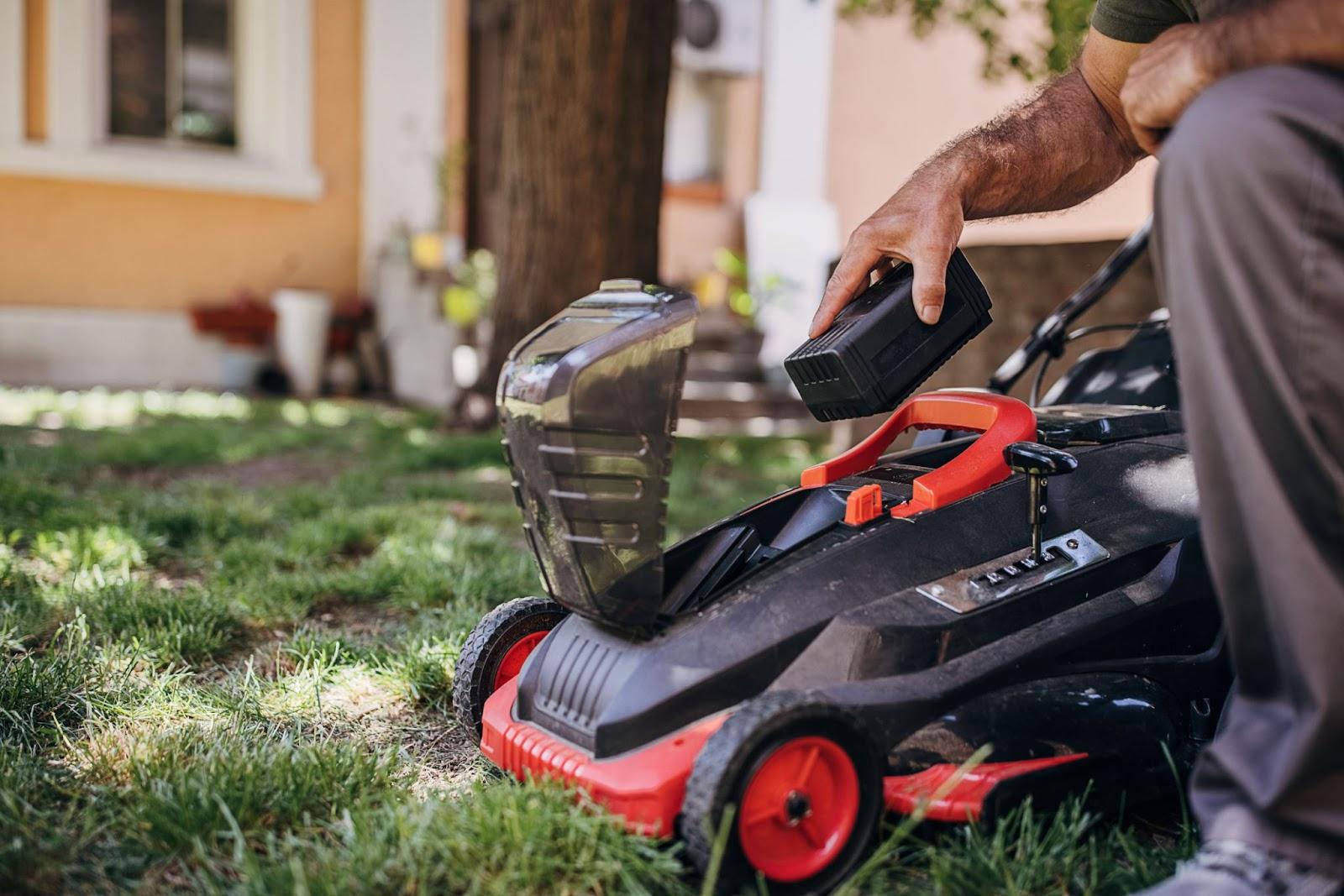 a person inserts a battery into their electric powered lawn mower