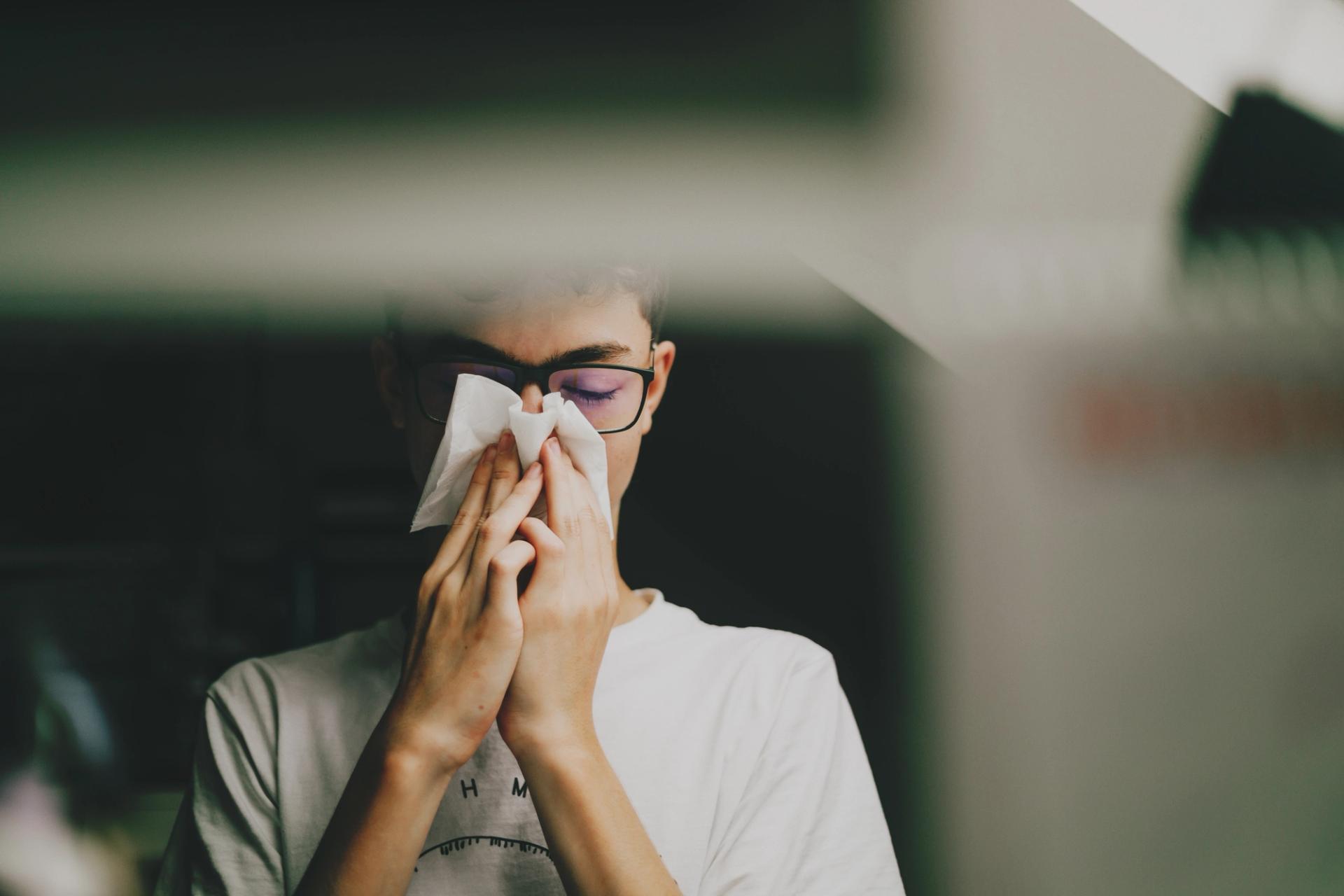 A man in a white T-shirt holding his handkerchief to his face.