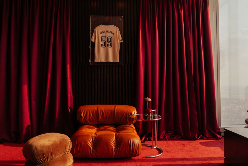 Cozy room with red velvet curtains, a framed sports jersey on a black wall, a tan leather chair, a matching footrest, and a small side table.