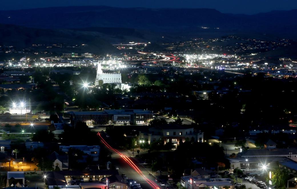 St. George Utah at night, with buildings glowing blue and green colors and mountains in the background.