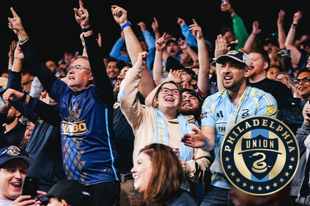 A group of enthusiastic Philadelphia Union soccer fans cheer in the stands, wearing team jerseys and scarves, creating an energetic and joyful atmosphere.