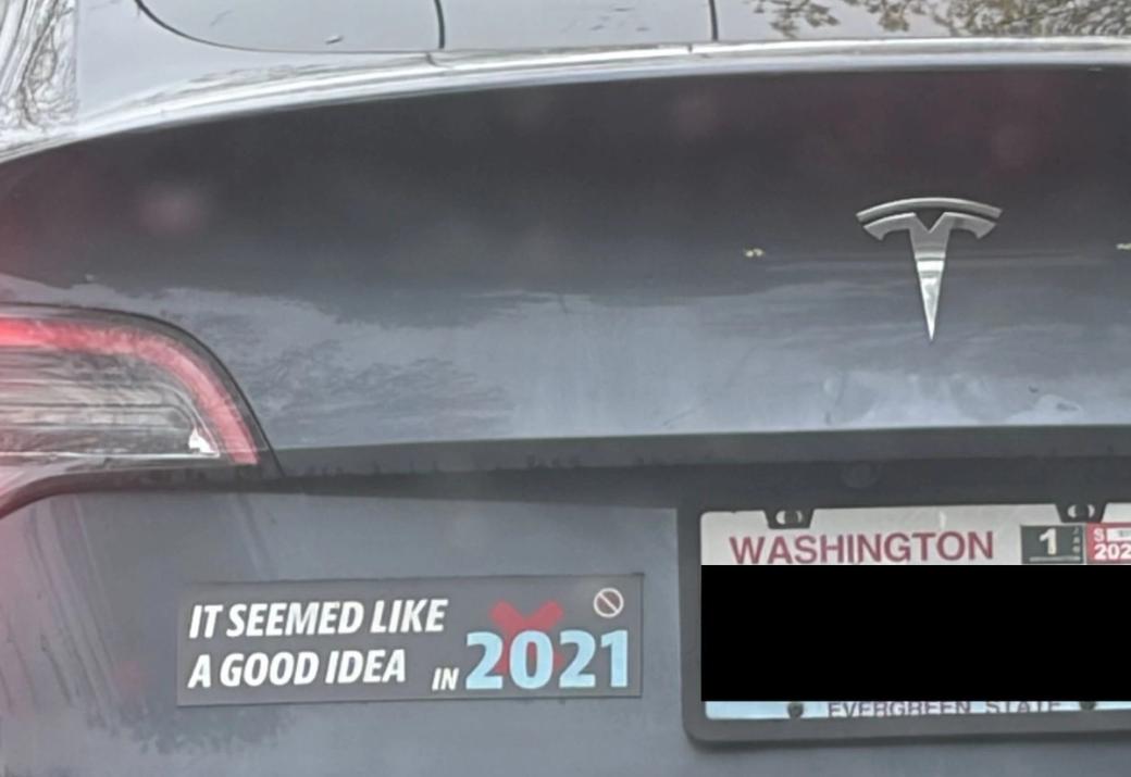 A photo of the back of a Tesla with a bumper sticker that reads ‘it seemed like a good idea in 2021.’