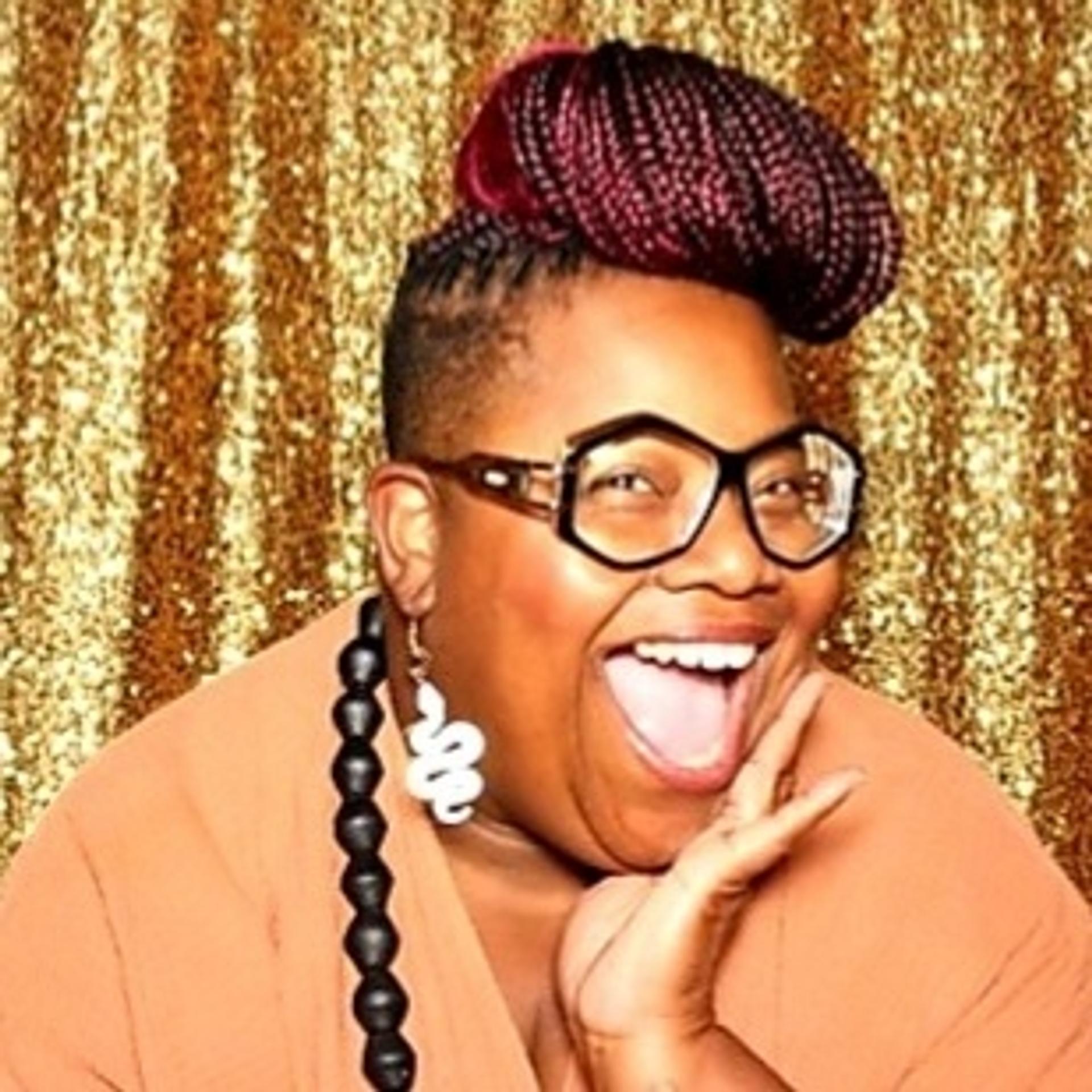 black woman with braids in a bun, fun geometric glasses, snack earrings, and a big smile with gold glitter backgroup