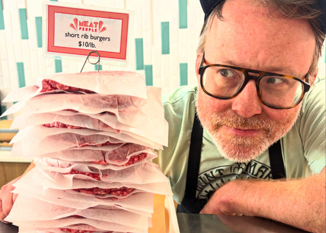 A man in glasses looking at a stack of meat patties.