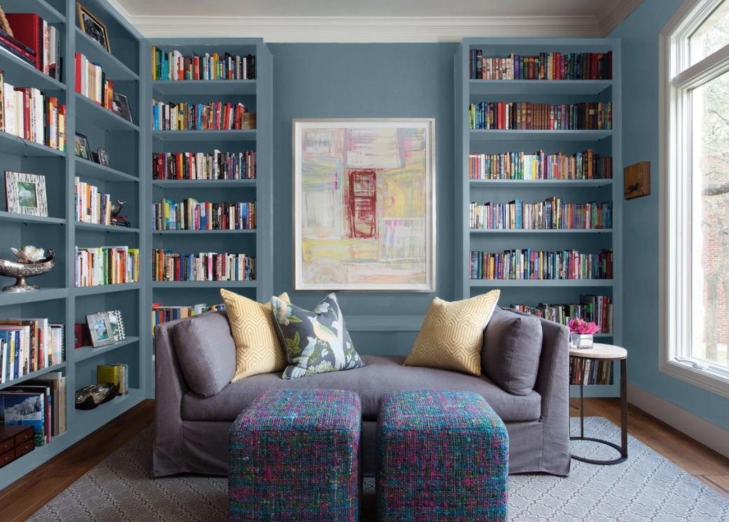 A gray couch sits in front of two walls of bookcases painted a medium, gray-ish blue.