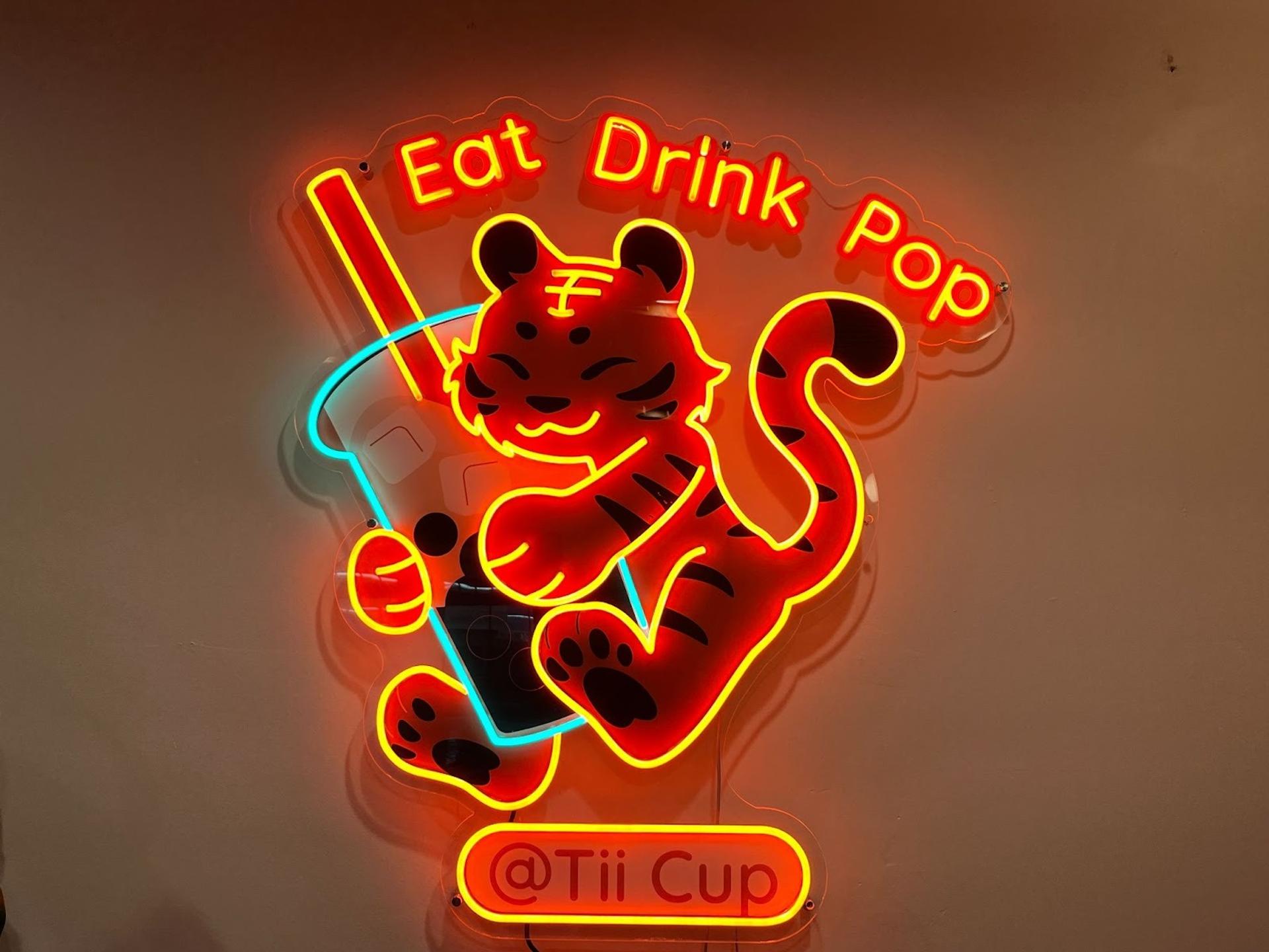 A neon sign with a tiger hugging a boba cup