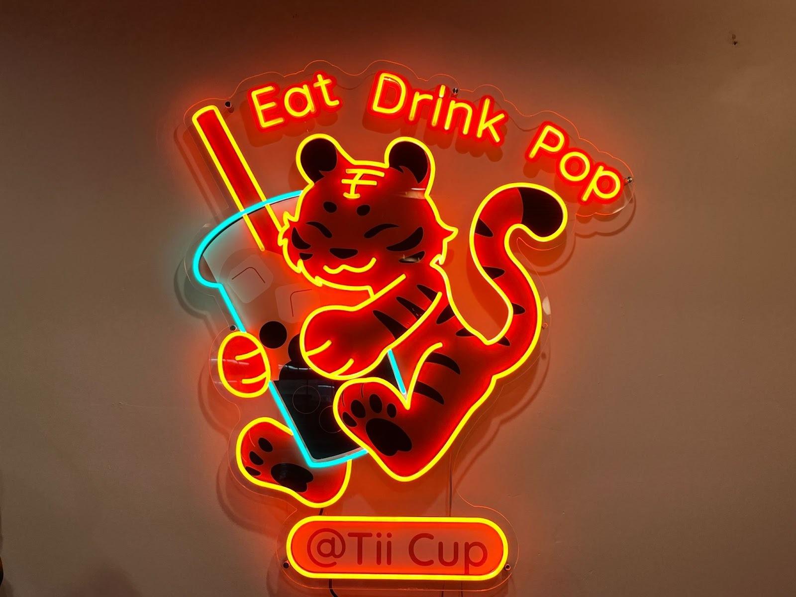 A neon sign with a tiger hugging a boba cup