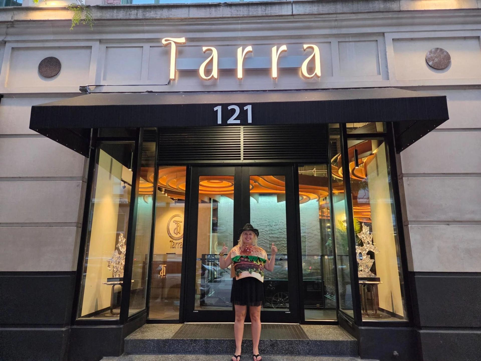 A woman standing under a lit up sign that says "Tarra" under the lit up sig is "121"