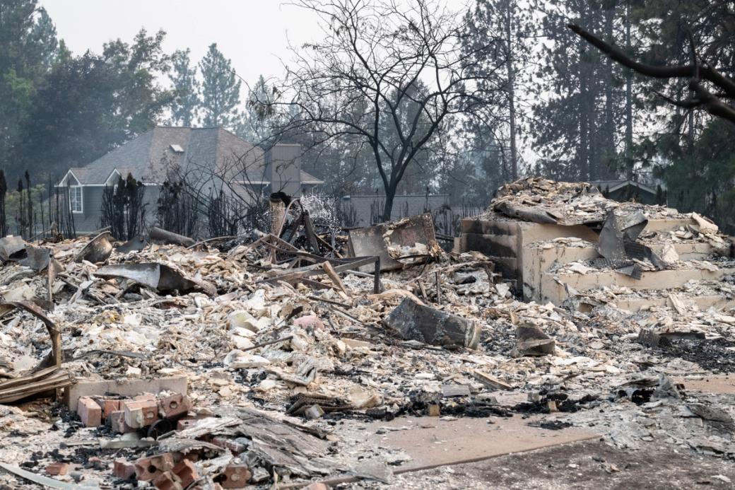 Ash covered remains of a home in Spokane with burned out trees in the background