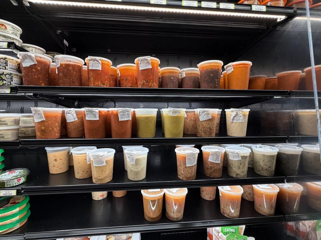 Tubs of soup in the refrigerator section of a grocery store.