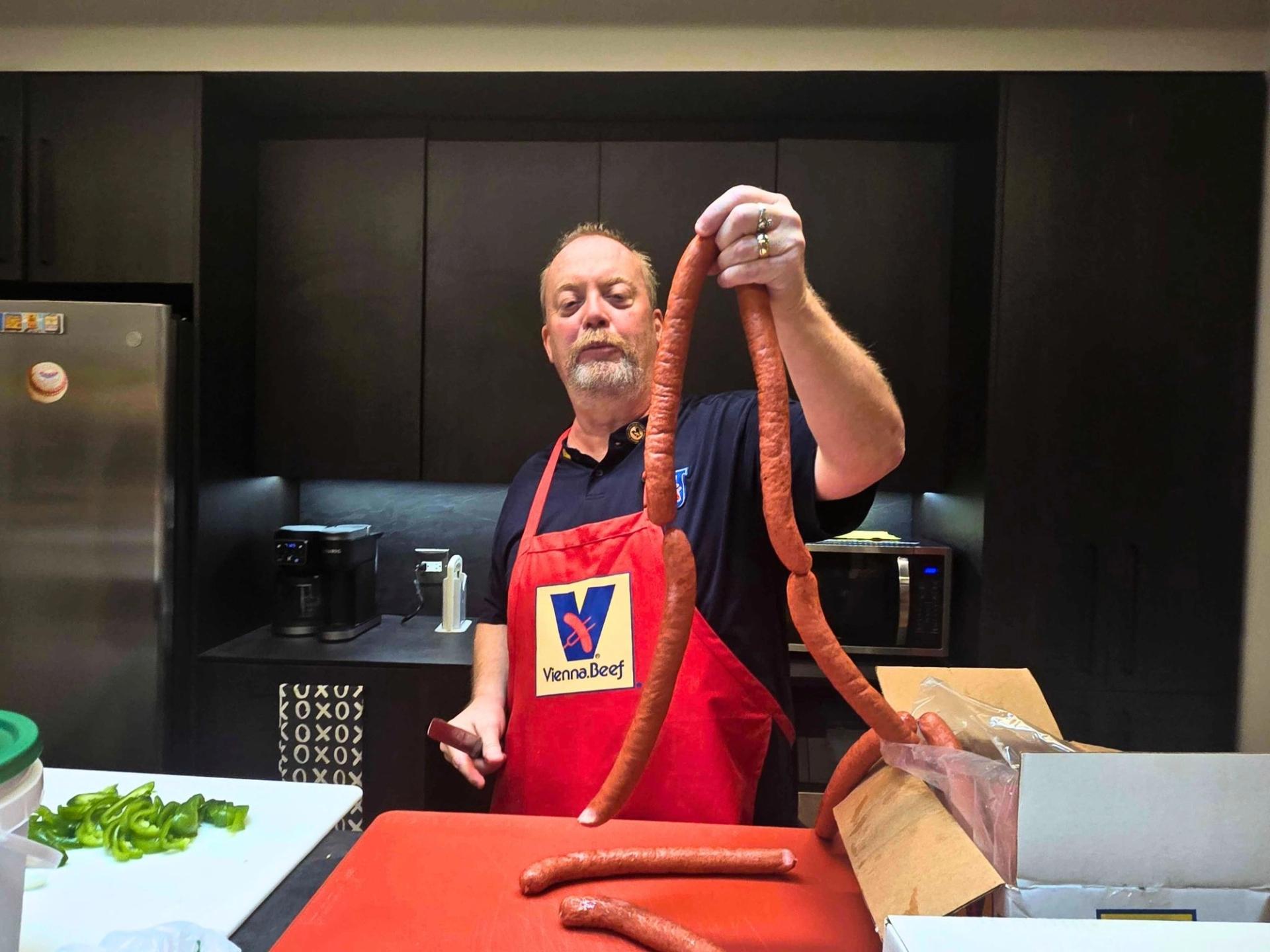 A man holding a link of hot dogs in a kitchen
