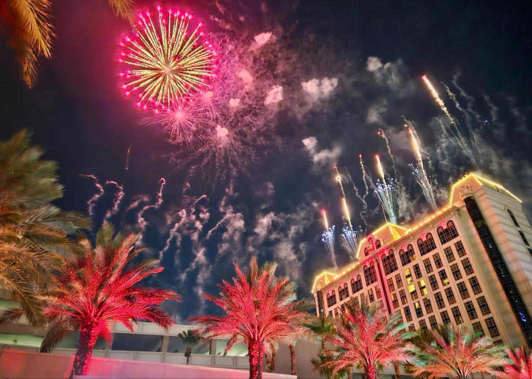 Pink, yellow and blue fireworks go off amid palm trees and hotels in Las Vegas.