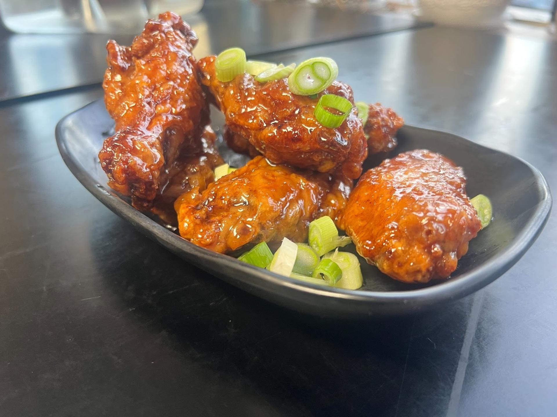 Saucy chicken wings with green onions on it served in a plate