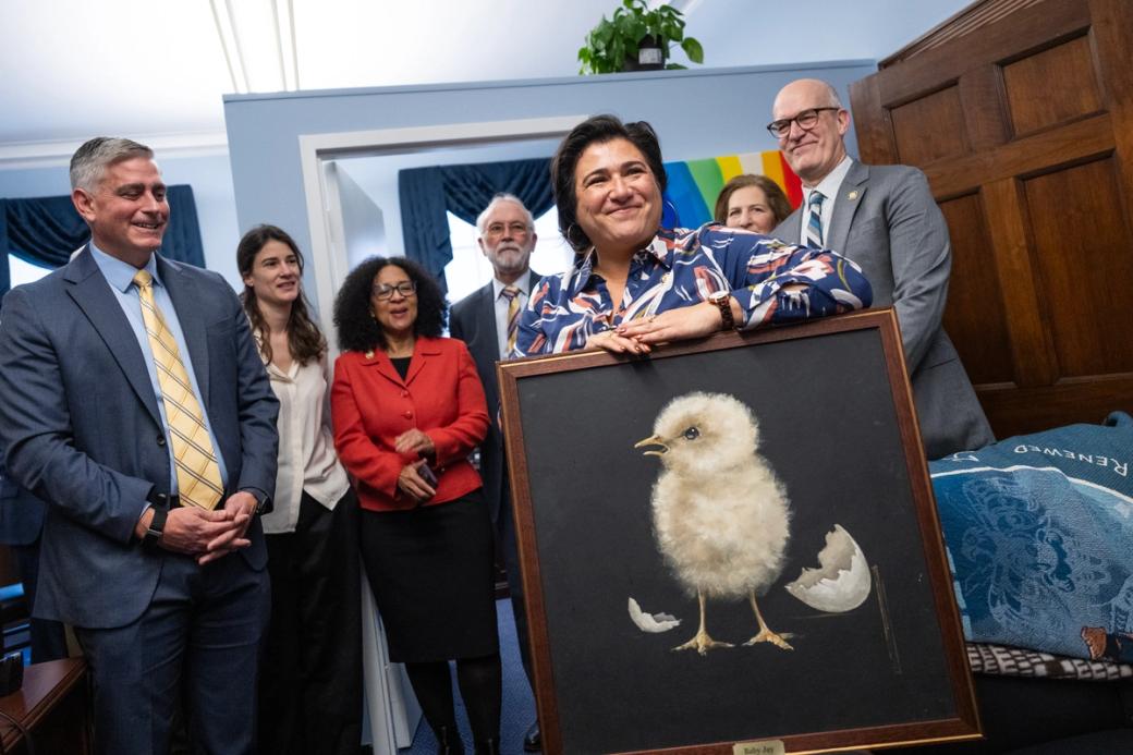 A person holding a painting of a chicken chick with people behind them