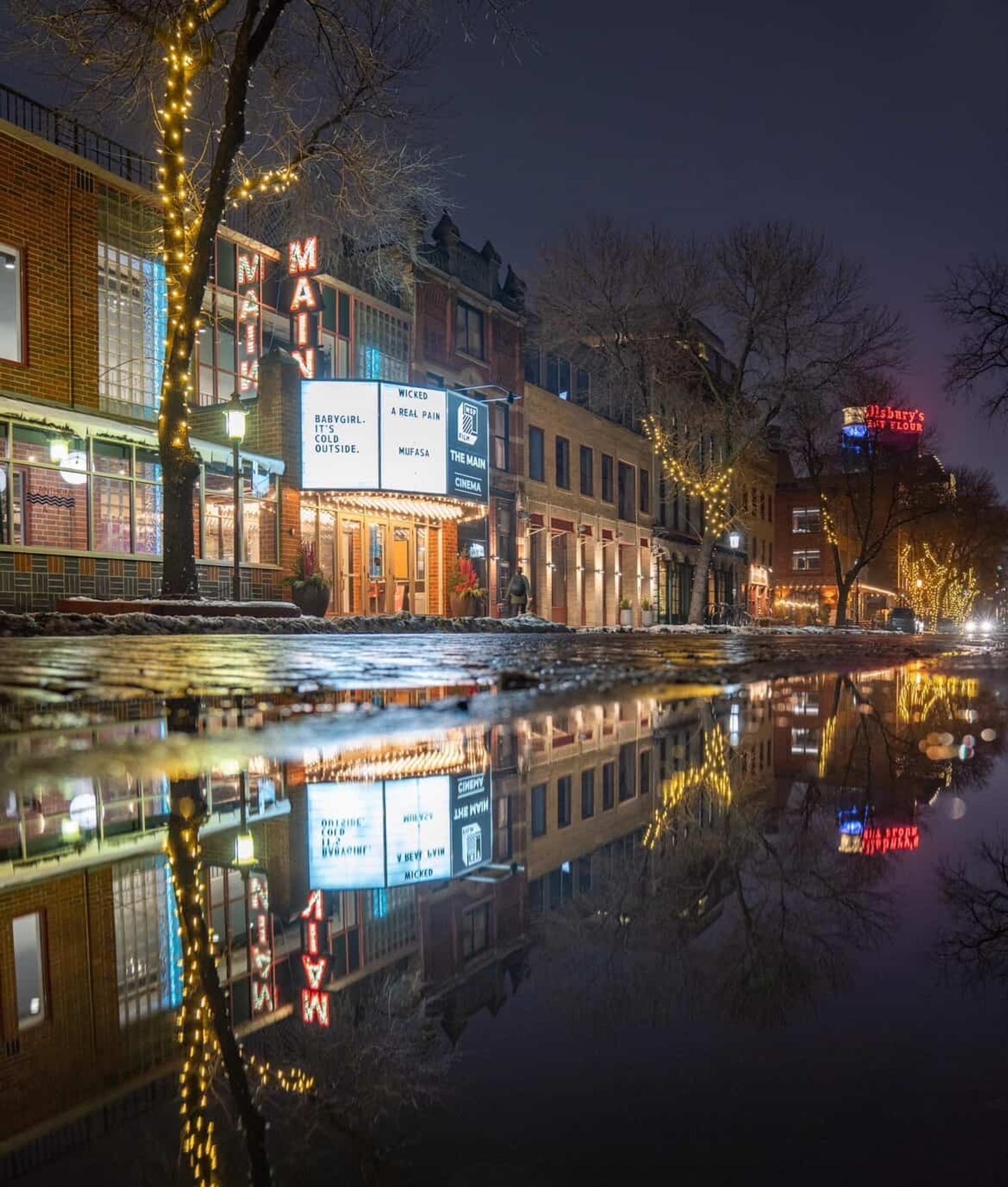 A wet street at night time outside of the The Main Theater