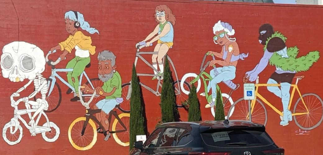 Mural of a people biking, with a skeleton on a ghost bike leading the way.