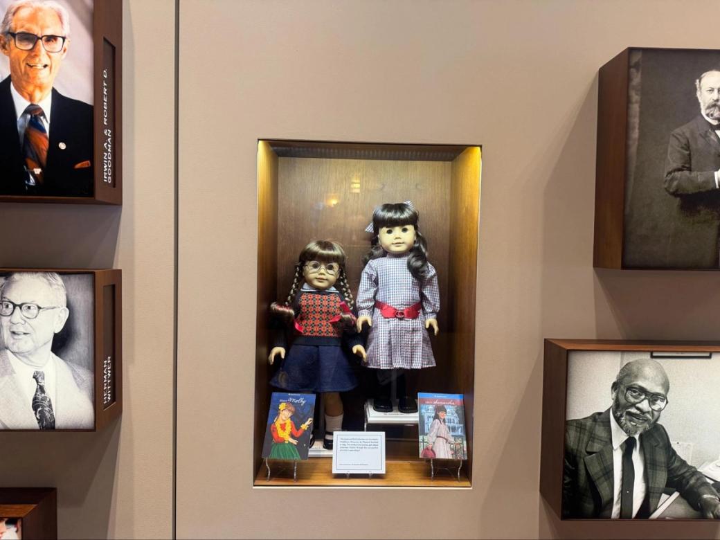Two dark-haired dolls in a wall alcove surrounded by photos.