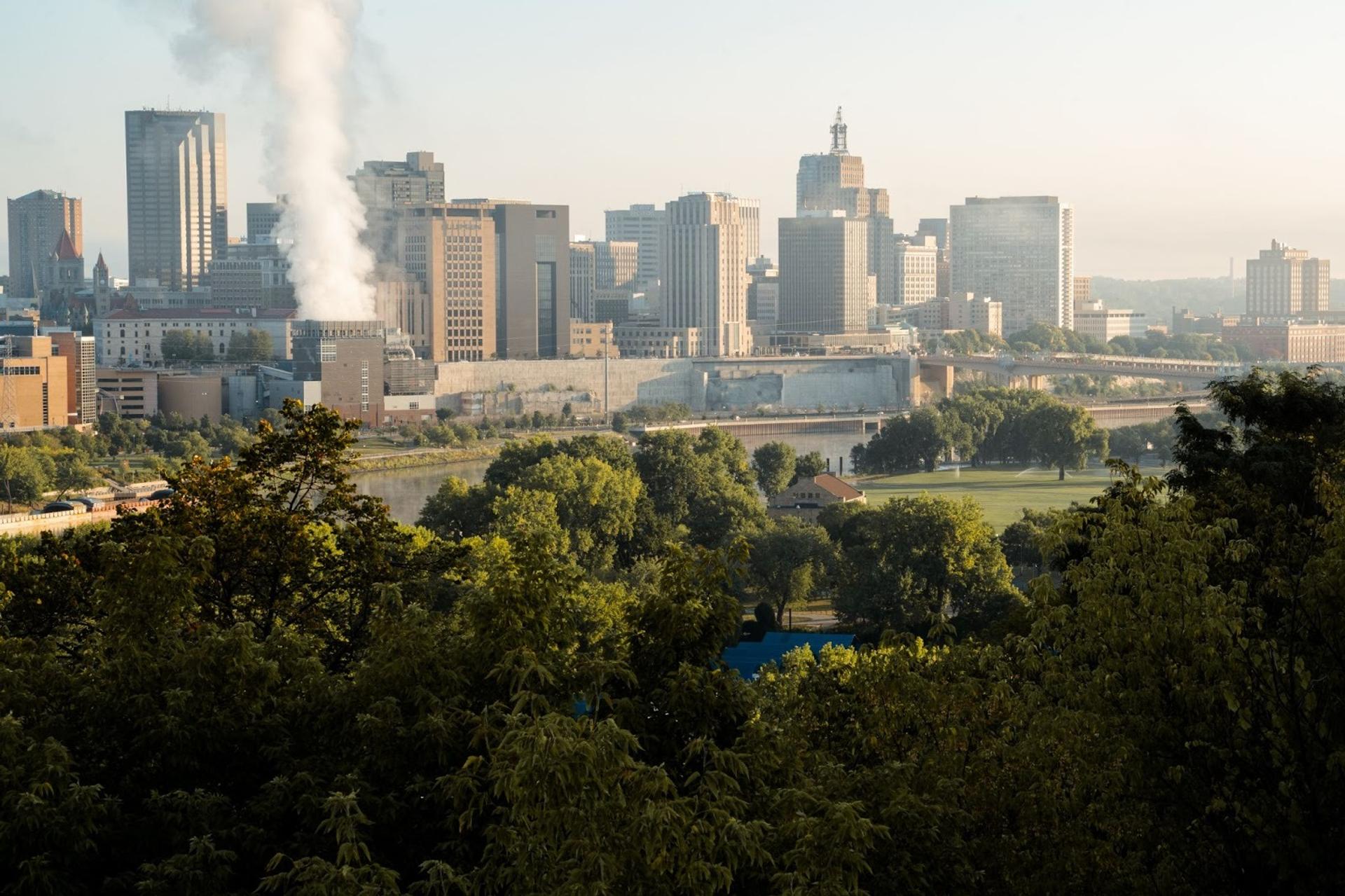 An overhead shot of the twin cities. There are trees in the foreground and the skyline in the background