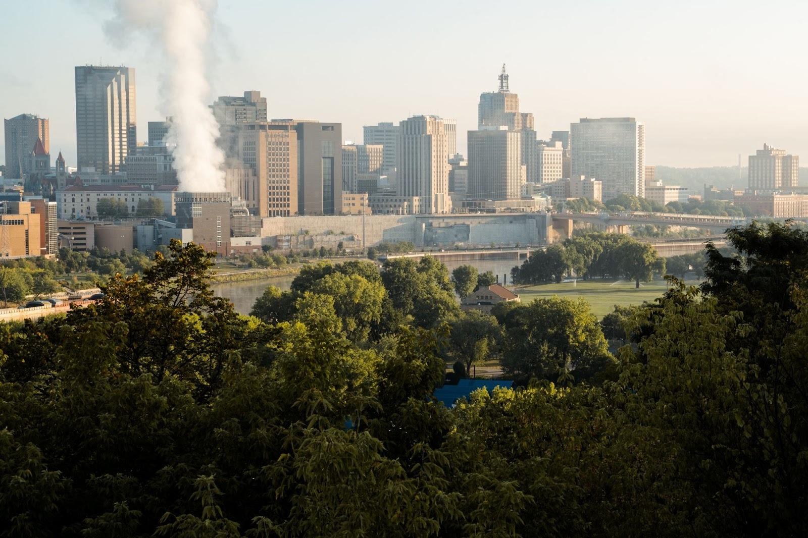 An overhead shot of the twin cities. There are trees in the foreground and the skyline in the background