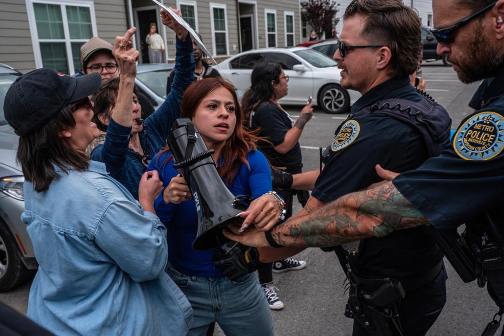 Police officers push back a group of women protesting. One holds a megaphone.