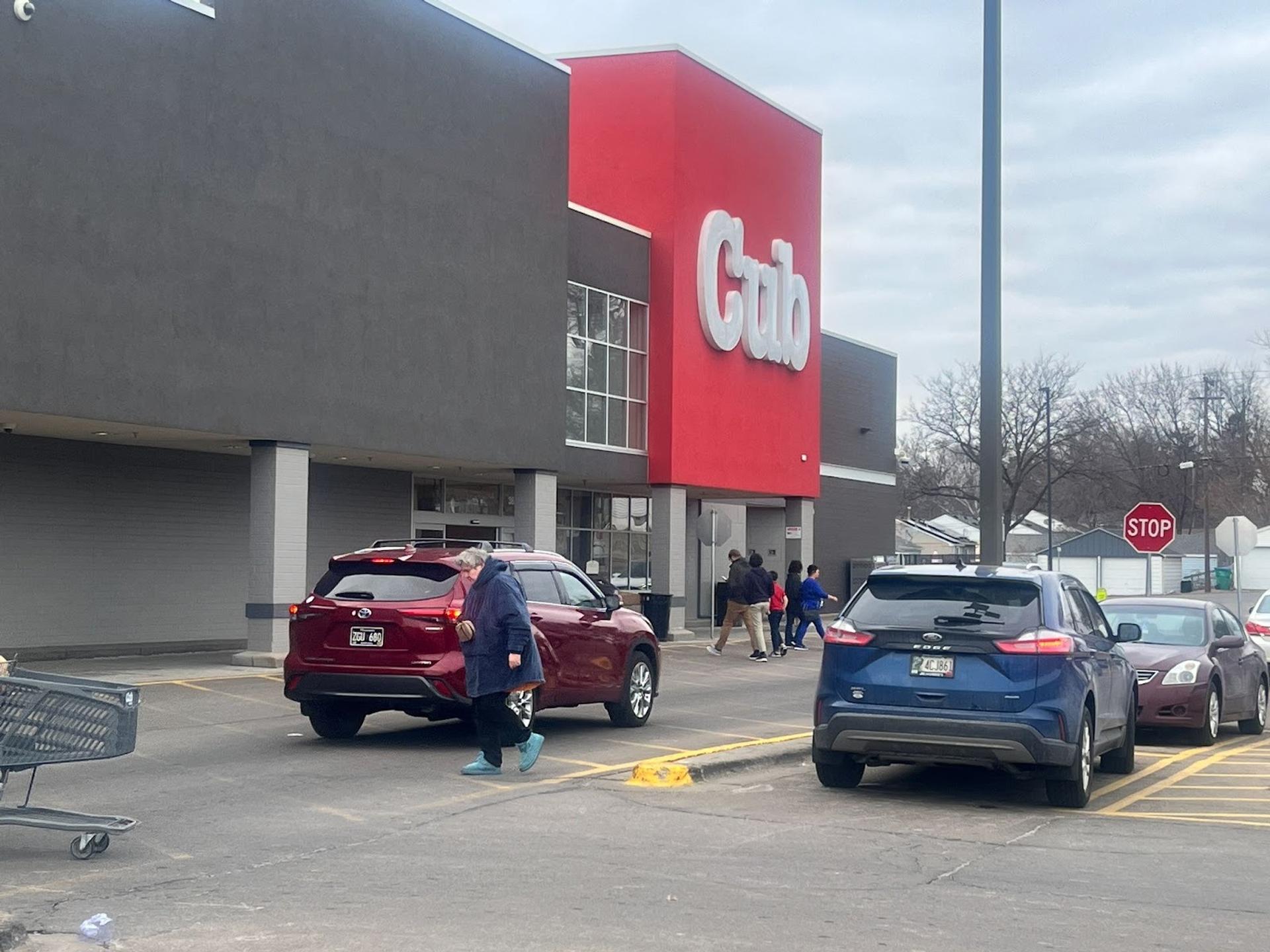 A view of the entrance of a store from the parking lot. Most of the building is a dark grey except for the entrance which is red and reads "Cub"