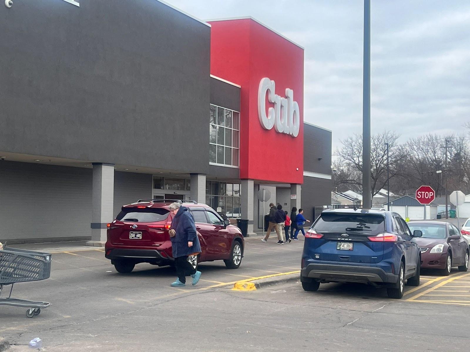 A view of the entrance of a store from the parking lot. Most of the building is a dark grey except for the entrance which is red and reads "Cub"