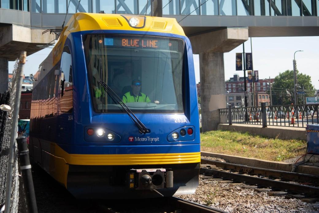 Looking at the front of a blue passenger train with driver in front seat